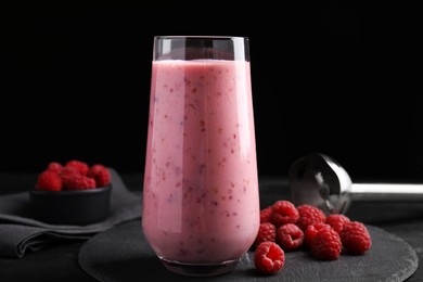 Photo of Glass of tasty raspberry smoothie on dark table against black background