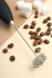 Milk frother wand, coffee beans and sugar cubes on color background, closeup