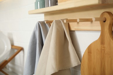 Photo of Different towels and wooden board hanging on rack in kitchen, closeup