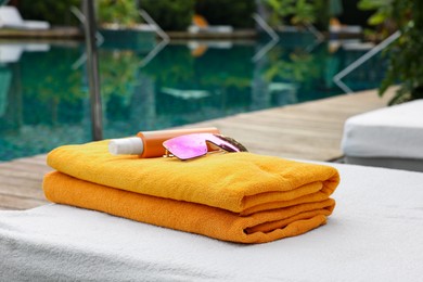 Photo of Beach towels, sunglasses and sunscreen on sun lounger near outdoor swimming pool. Luxury resort