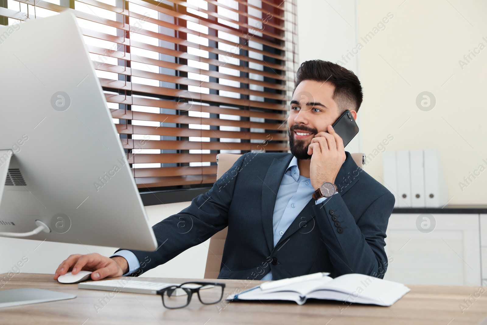 Photo of Handsome businessman talking on phone while working with computer at table in office