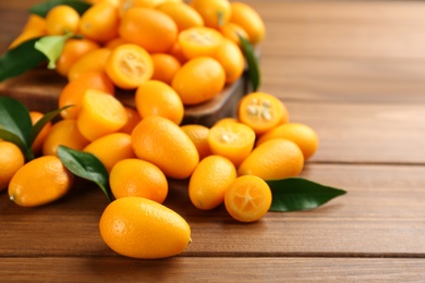 Photo of Fresh ripe kumquats with green leaves on wooden table
