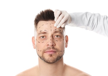 Doctor examining man's face before plastic surgery operation on white background