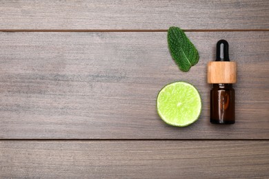 Photo of Bottle of citrus essential oil and fresh lime on wooden table, flat lay. Space for text