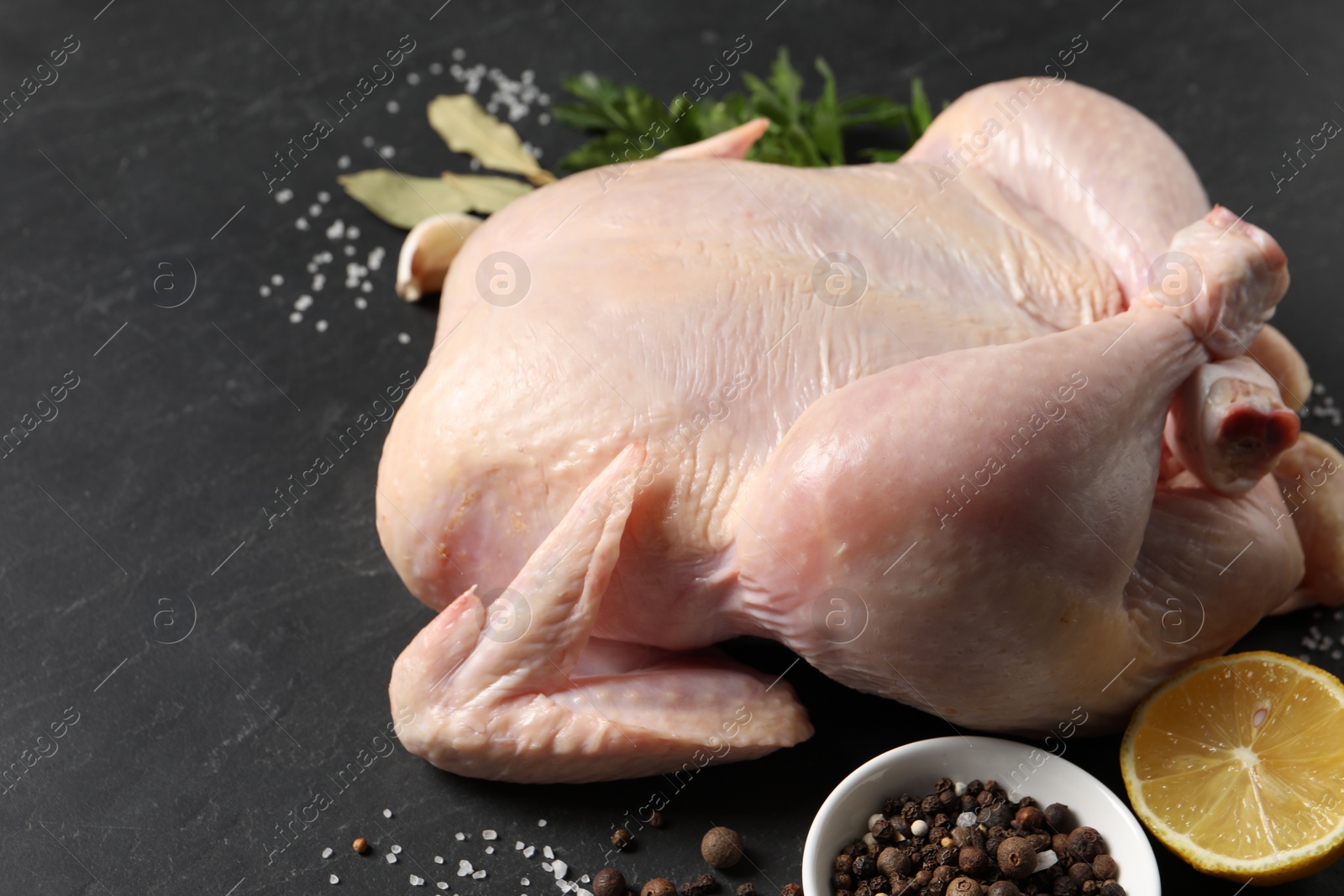 Photo of Fresh raw chicken with spices and lemon on black textured table