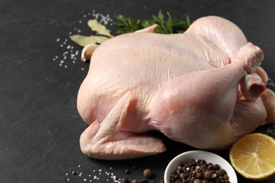 Photo of Fresh raw chicken with spices and lemon on black textured table