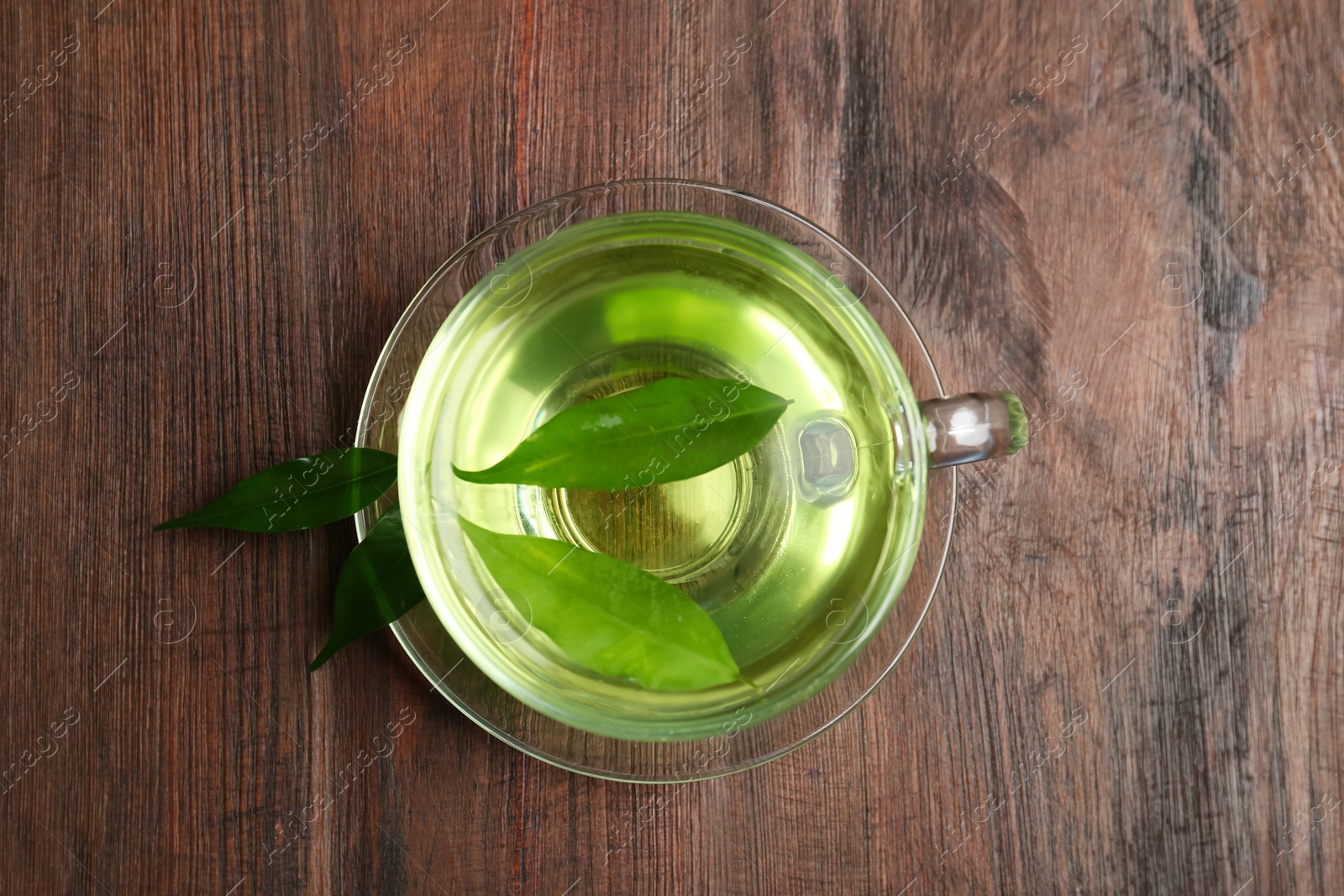 Photo of Cup of aromatic green tea and leaves on wooden table, top view