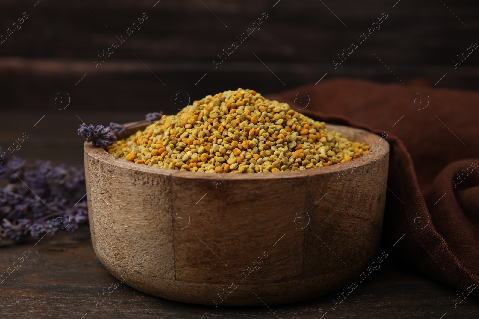 Photo of Fresh bee pollen granules in bowl and lavender on wooden table, closeup