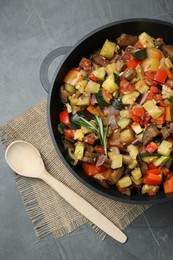 Photo of Delicious ratatouille in baking dish and wooden spoon on grey table, flat lay