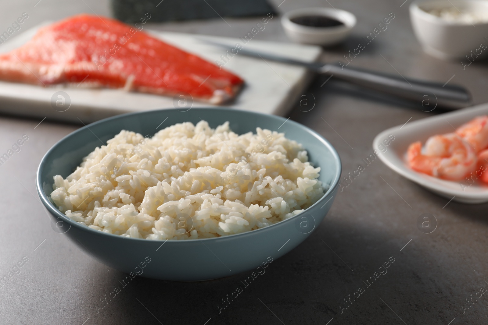 Photo of Cooked rice in bowl for sushi on grey table, closeup
