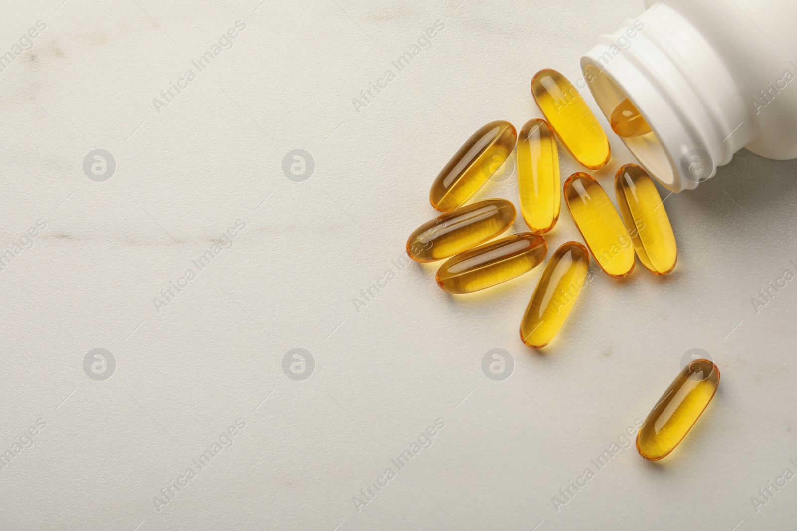 Photo of Overturned bottle with dietary supplement capsules on white table, flat lay. Space for text