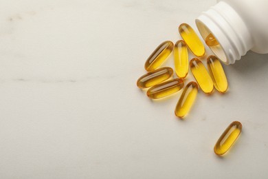 Photo of Overturned bottle with dietary supplement capsules on white table, flat lay. Space for text