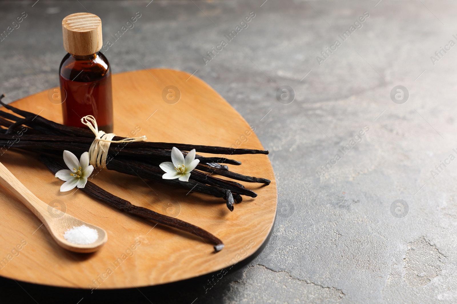 Photo of Bunch of vanilla pods, flowers, sugar and bottle with essential oil on grey textured table, closeup. Space for text