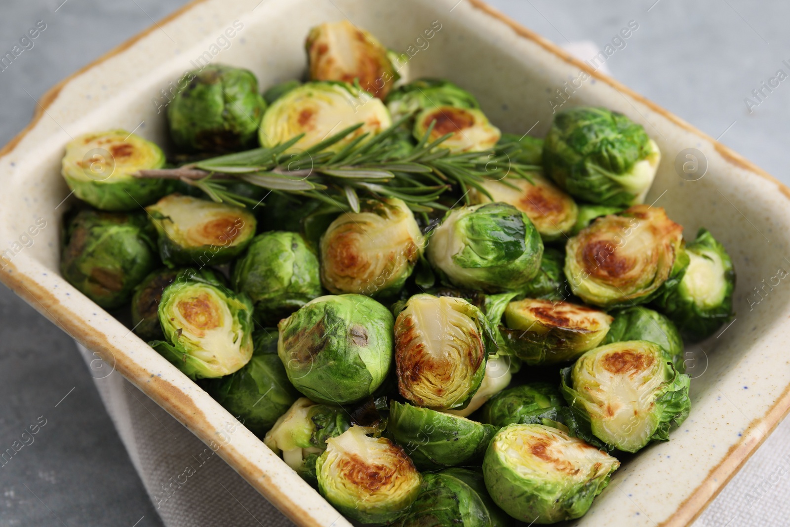 Photo of Delicious roasted Brussels sprouts and rosemary in baking dish on grey table, closeup