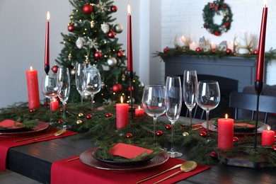 Photo of Elegant Christmas table setting with dishware and burning candles in festively decorated room