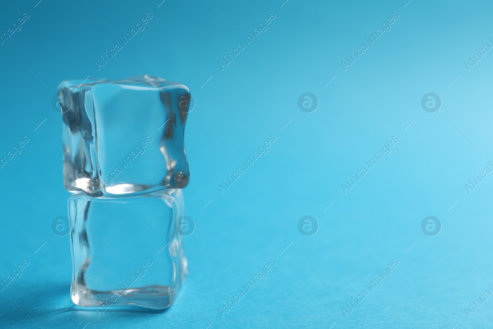 Photo of Crystal clear ice cubes on blue background, closeup. Space for text