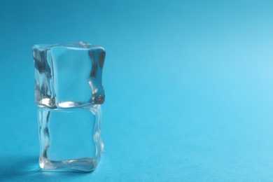 Photo of Crystal clear ice cubes on blue background, closeup. Space for text