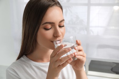 Woman drinking tap water from glass at home, closeup