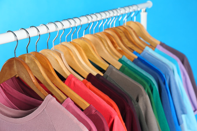 Photo of Colorful clothes on hangers against light blue background