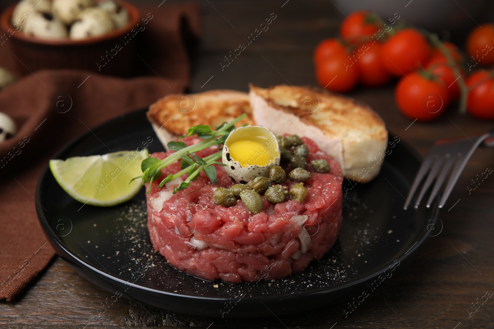 Photo of Tasty beef steak tartare served with quail egg and other accompaniments on wooden table