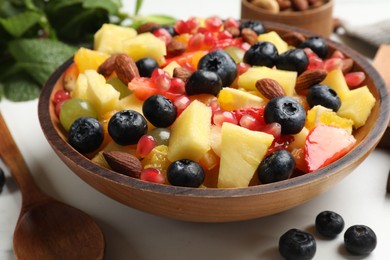 Delicious fruit salad in bowl, berries, fresh mint and nuts on white marble table, closeup