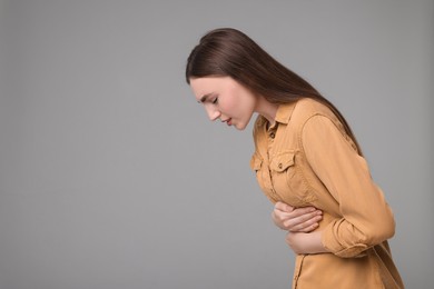 Photo of Young woman suffering from stomach pain on grey background. Space for text