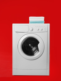 Photo of Modern washing machine with stack of towels on red background. Laundry day