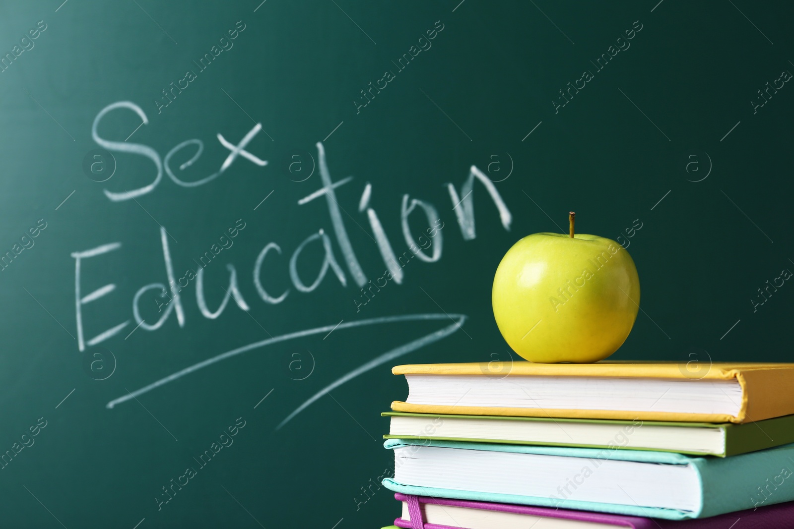 Photo of Books and apple near chalkboard with phrase "Sex education"