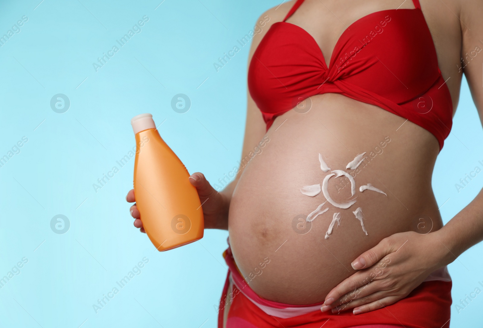 Photo of Young pregnant woman with sun protection cream on light blue background, closeup