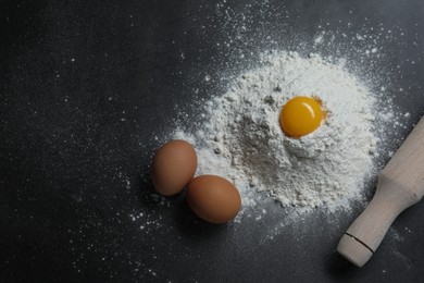 Photo of Flour, rolling pin and eggs on black table, flat lay