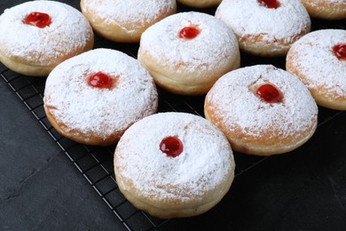 Many delicious donuts with jelly and powdered sugar on black table