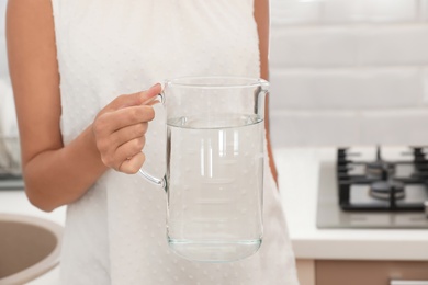 Photo of Woman holding glass jug with water in kitchen, closeup