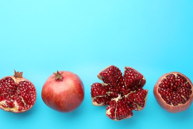 Whole and cut fresh pomegranates on light blue background, flat lay. Space for text