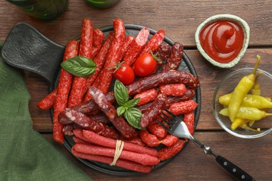 Photo of Different thin dry smoked sausages, sauce and tomatoes on wooden table, flat lay