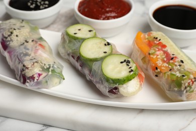 Different delicious rolls wrapped in rice paper on white marble board, closeup