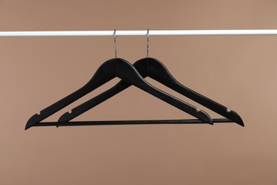 Photo of Black clothes hangers on rack against light brown background