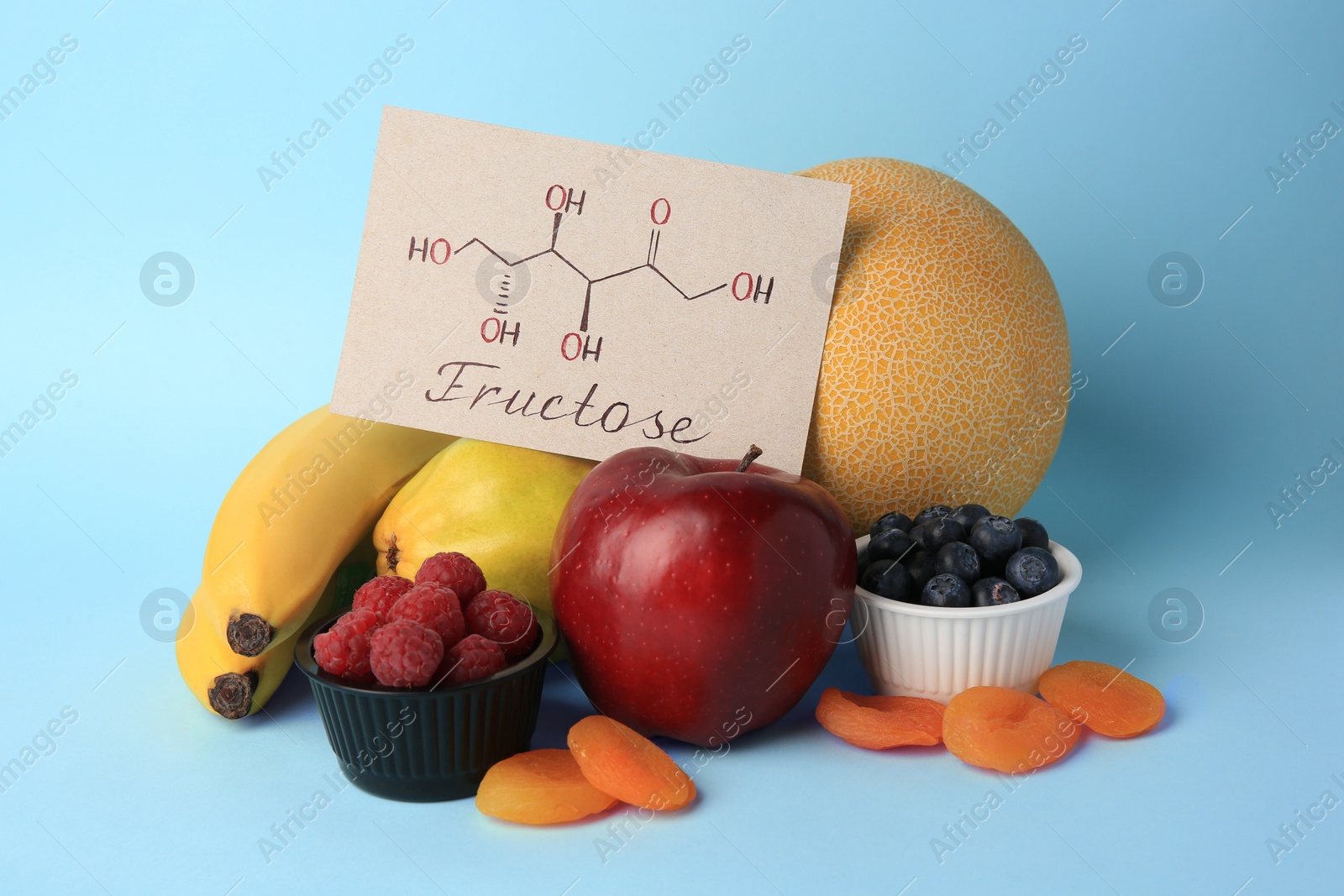 Photo of Card with word Fructose, delicious ripe fruits, berries and dried apricots on light blue background