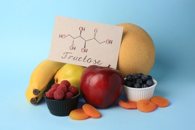 Photo of Card with word Fructose, delicious ripe fruits, berries and dried apricots on light blue background