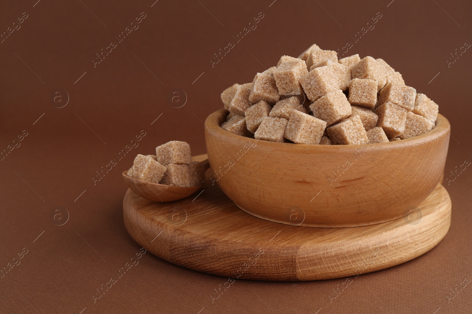 Photo of Brown sugar cubes in bowl and spoon on color background. Space for text