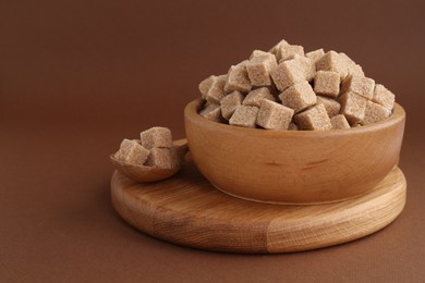 Photo of Brown sugar cubes in bowl and spoon on color background. Space for text