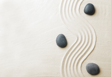 Photo of Zen garden stones on sand with pattern, top view. Space for text