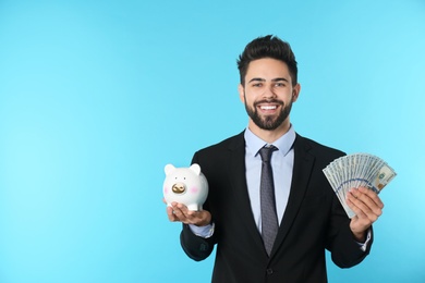 Photo of Portrait of happy young businessman with money and piggy bank on color background. Space for text