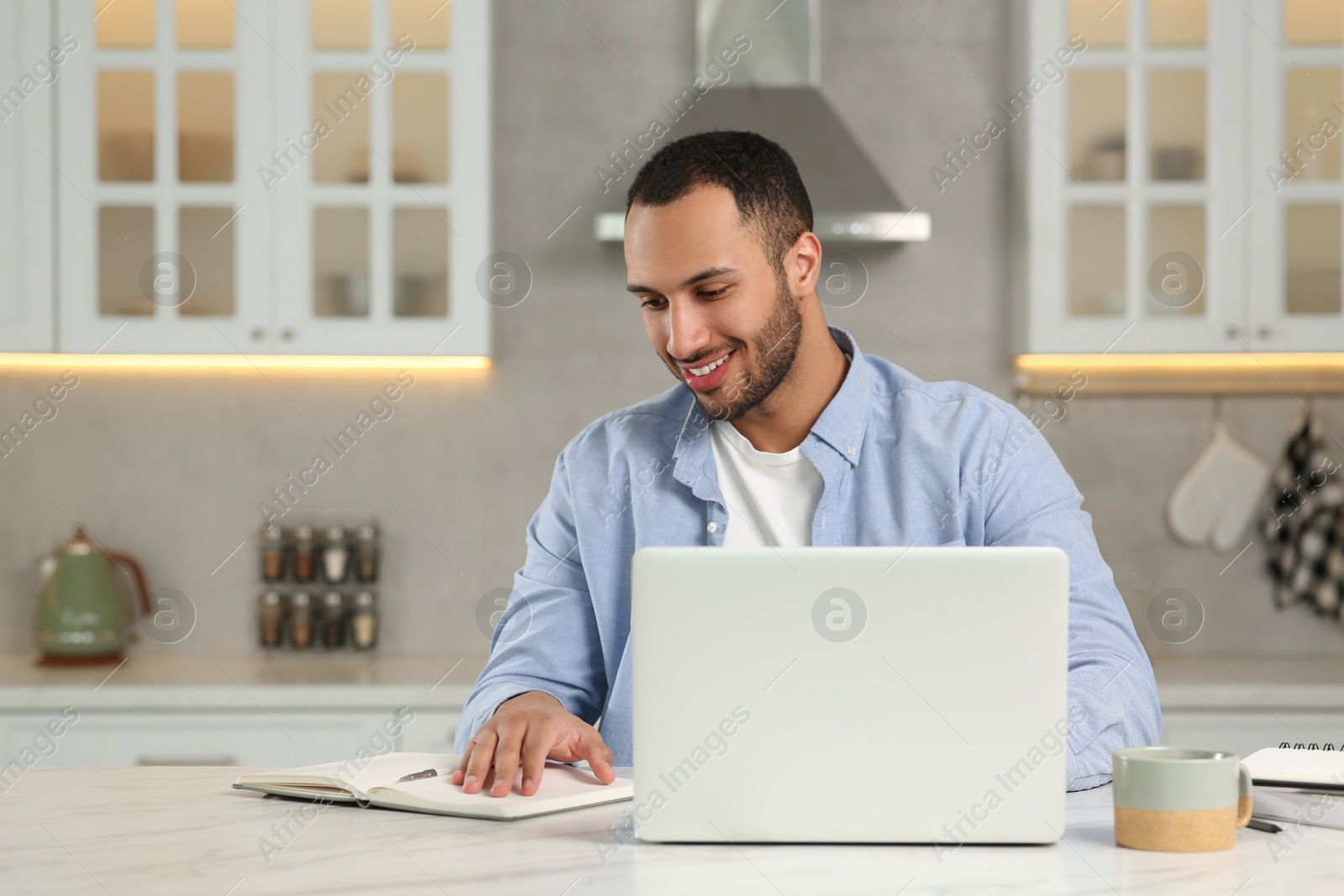 Photo of Young man working on laptop at desk in kitchen. Home office