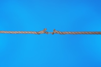 Stretched frayed rope breaking on color background