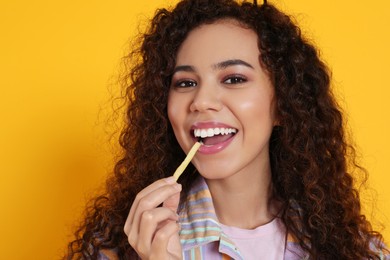 Photo of African American woman eating French fries on yellow background