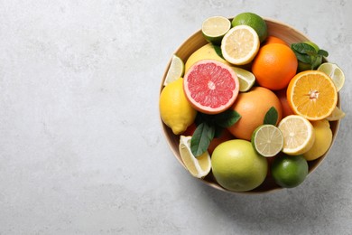 Photo of Different fresh citrus fruits and leaves in bowl on light table, top view. Space for text