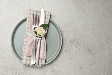 Plate with fabric napkin, cutlery and flower on light grey table, top view. Space for text
