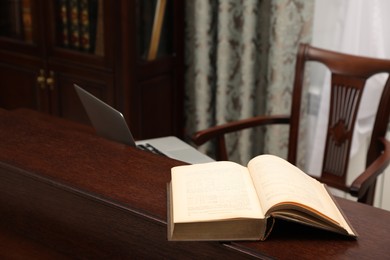 Photo of Old book and laptop on wooden table in library reading room