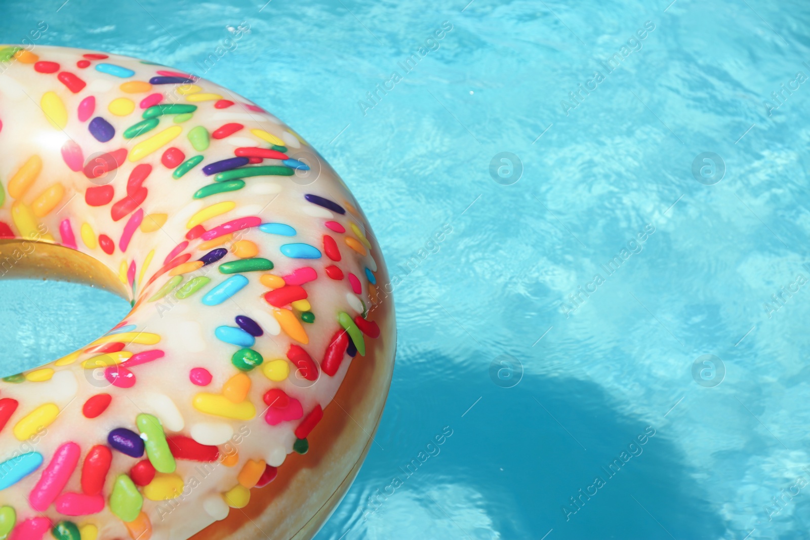 Photo of Bright inflatable doughnut ring floating in swimming pool on sunny day. Space for text