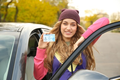 Photo of Young woman holding driving license near open car
